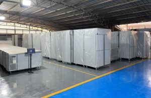Large inventory of industrial freezers and commercial kitchen equipment packaged in plastic on a polished factory floor, organized for wholesale distribution.